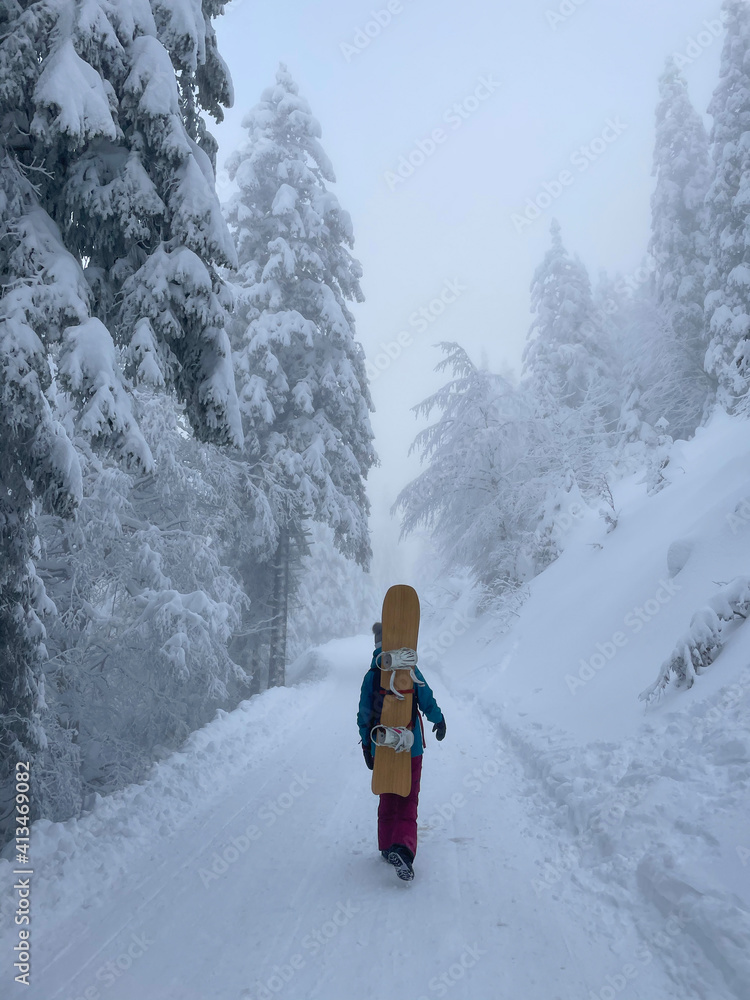 垂直：一名无法辨认的女子背着滑雪板沿着一条空荡荡的道路徒步旅行。