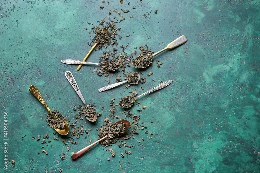 Spoons with dry tea leaves on color background