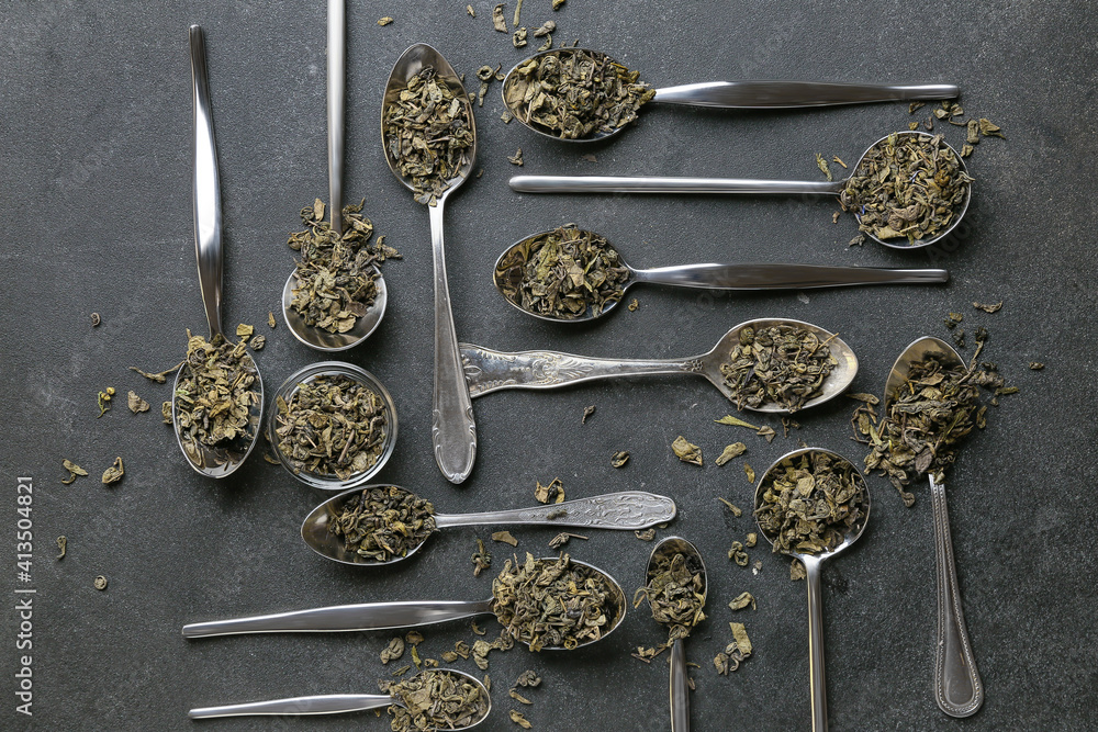 Spoons and bowl with dry tea leaves on dark background