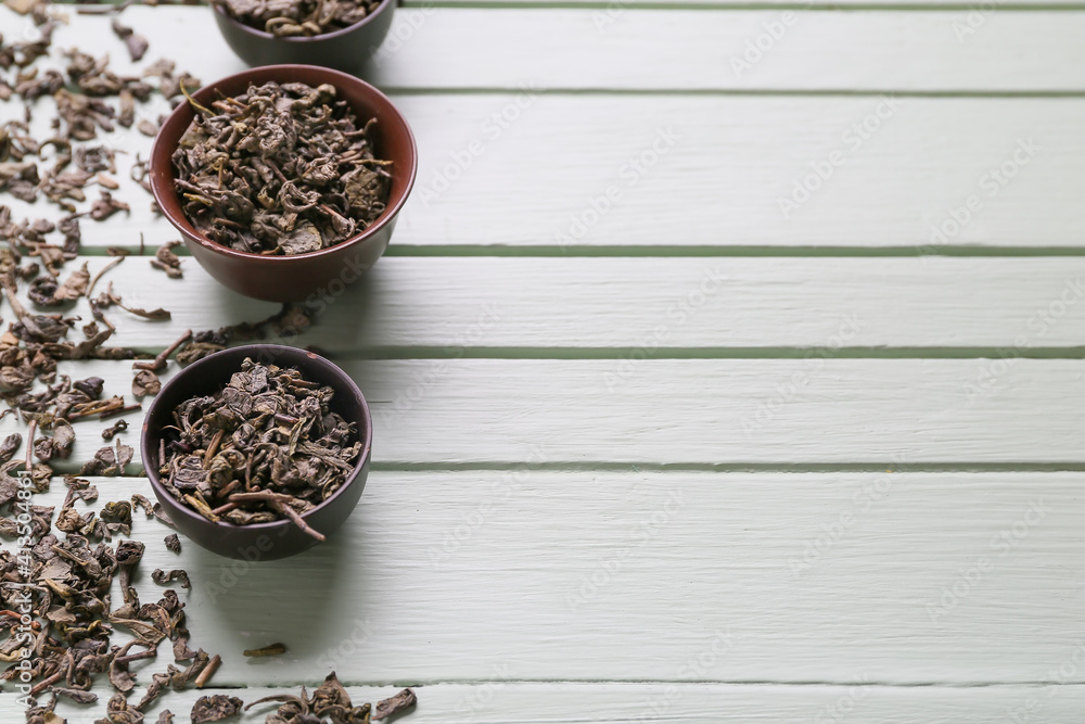 Bowls with dry tea leaves on wooden background