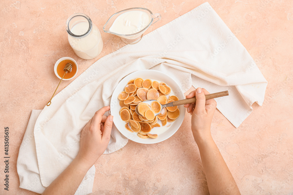 Woman eating tasty pancakes with milk on color background