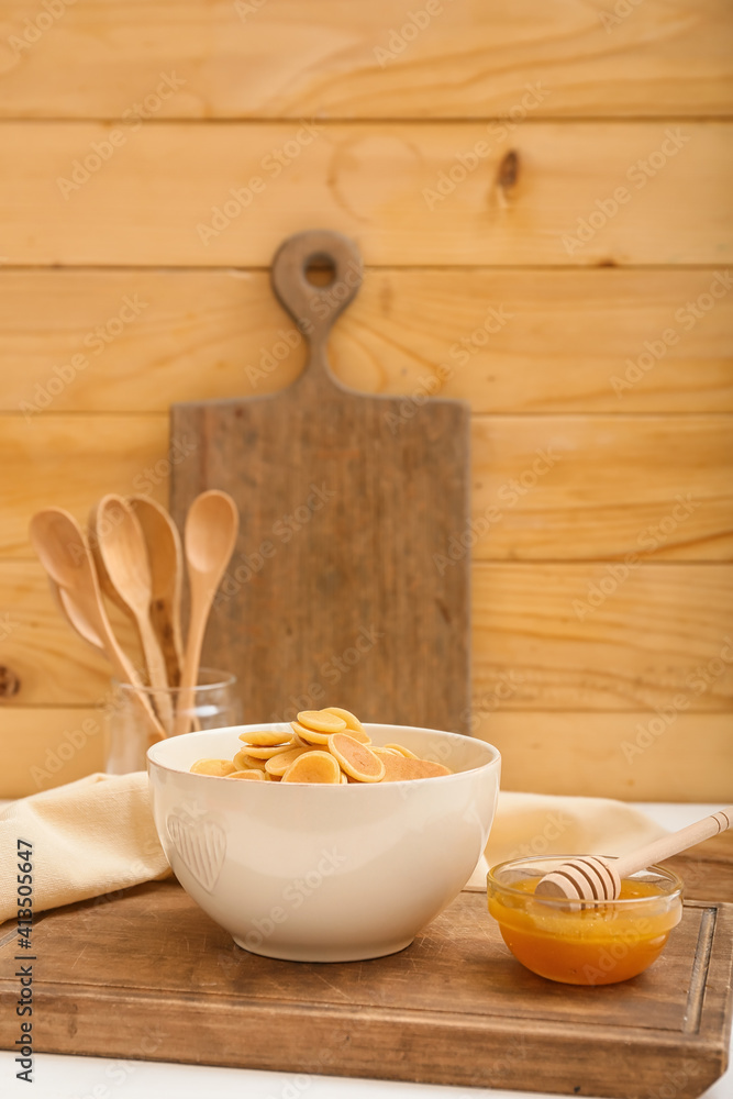 Bowl with tasty pancakes and honey on wooden background