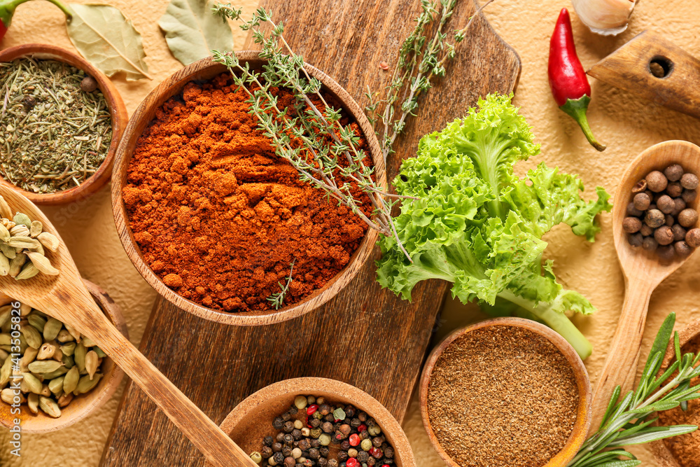 Bowls and spoons with different spices and herbs on color background, closeup