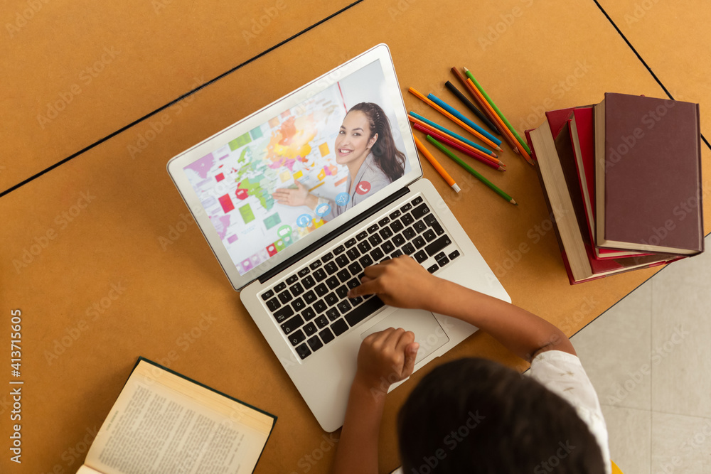 Overhead view of male student having a video call with female teacher on laptop at school