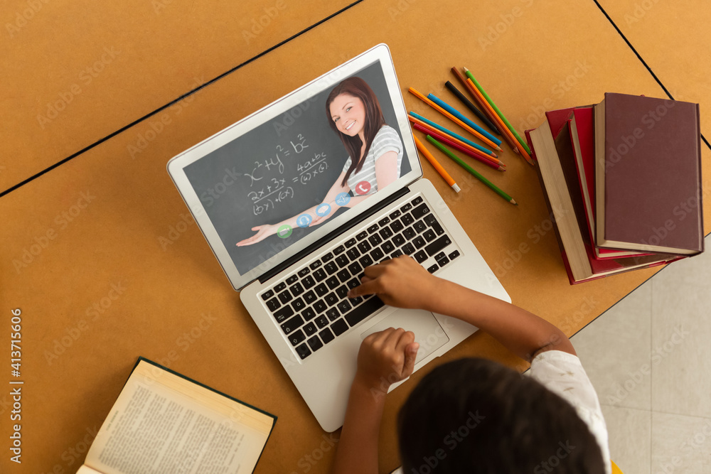 Overhead view of male student having a video call with female teacher on laptop at school