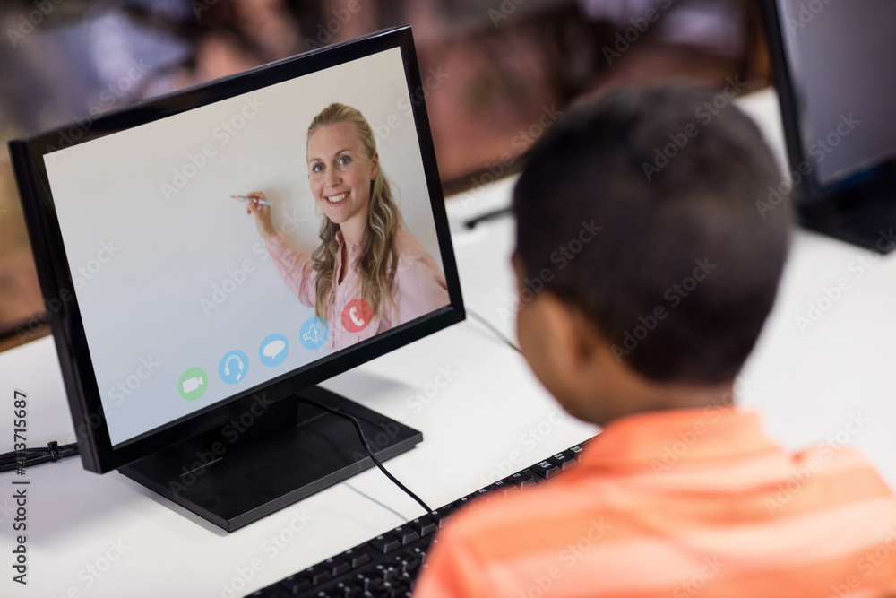 Male student having a video call with female teacher on computer at school