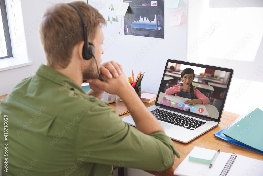 Male teacher wearing headphones having a video call with female student on laptop at home