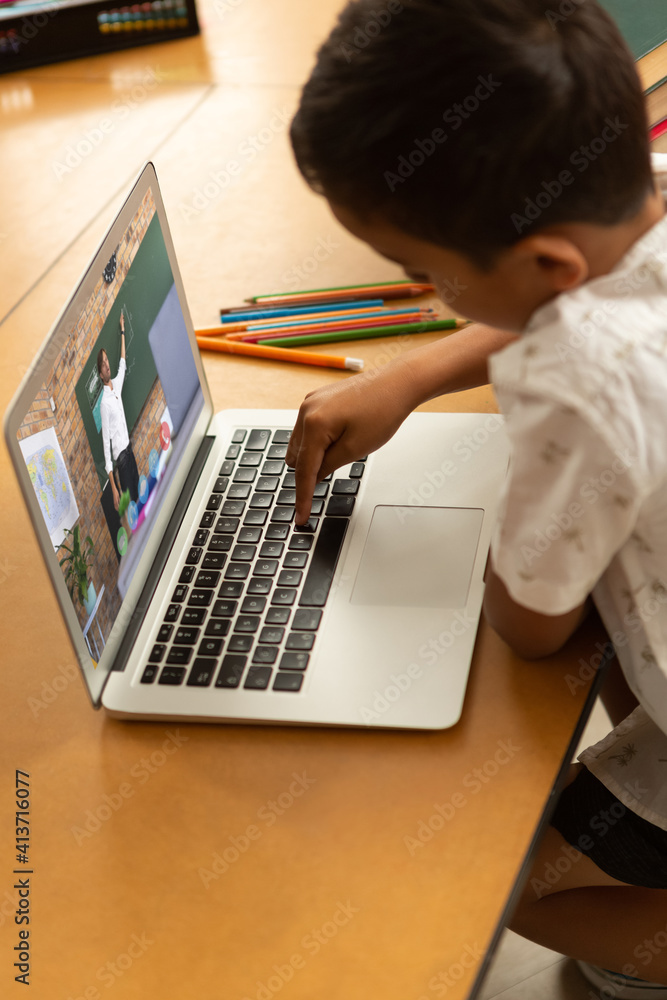 Male student having a video call with male teacher on laptop at school