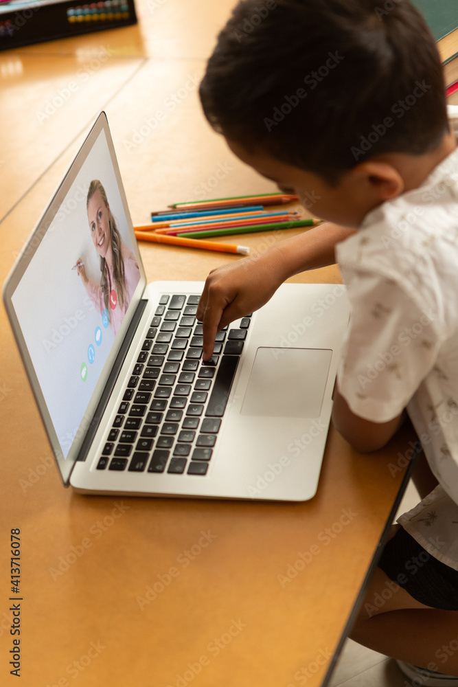 Male student having a video call with female teacher on laptop at school