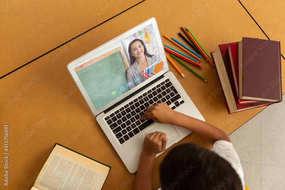 Overhead view of male student having a video call with female teacher on laptop at school