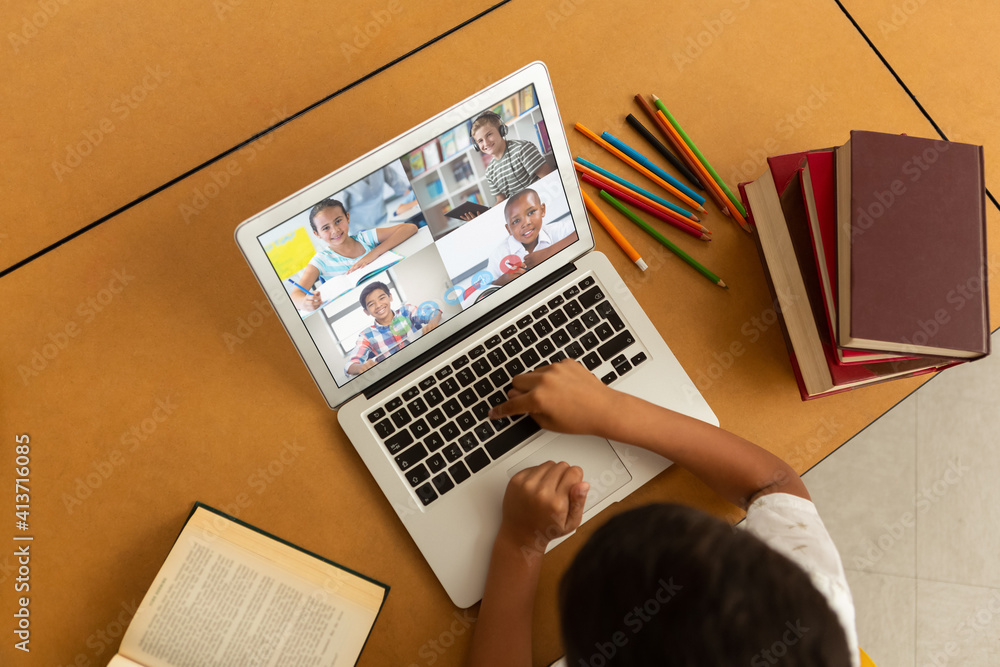 Overhead view of male student having a video conference with multiple students on laptop at school