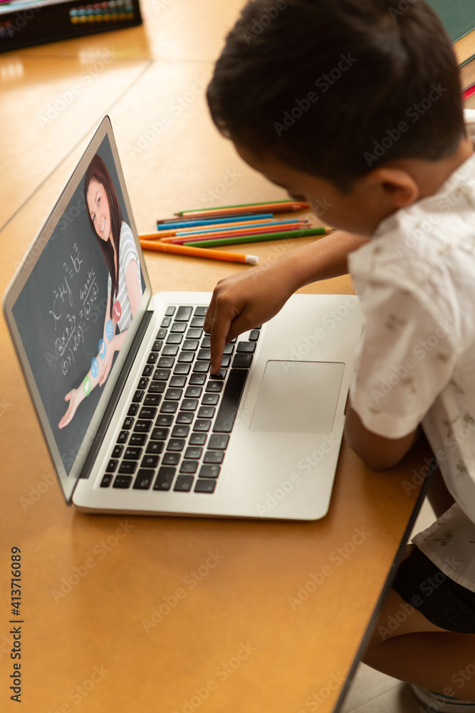 Male student having a video call with female teacher on laptop at school