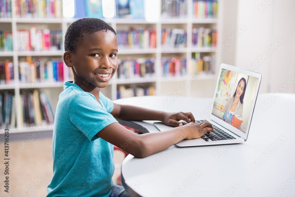 Portrait of male african american student having a video call with female teacher on laptop at libra