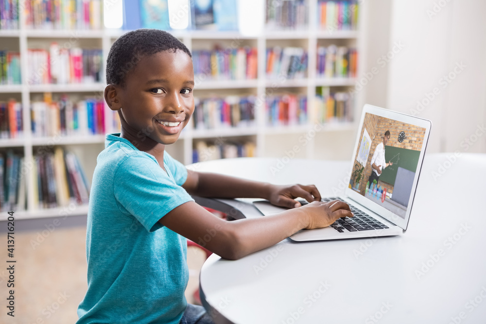 Portrait of male african american student having a video call with male teacher on laptop at library