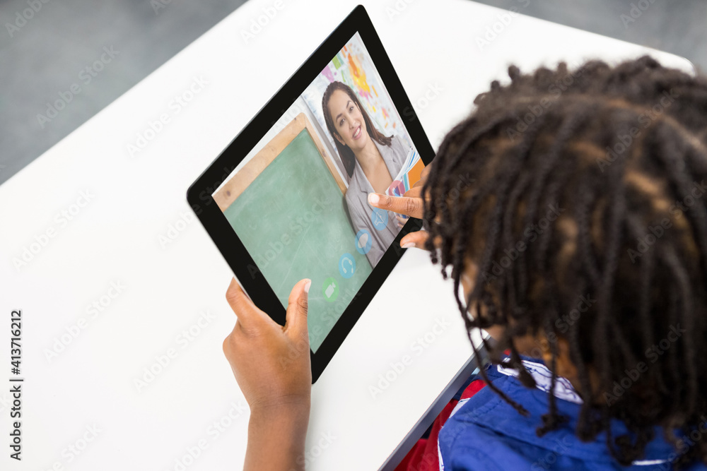 Male student having a video call with female teacher on digital tablet at school