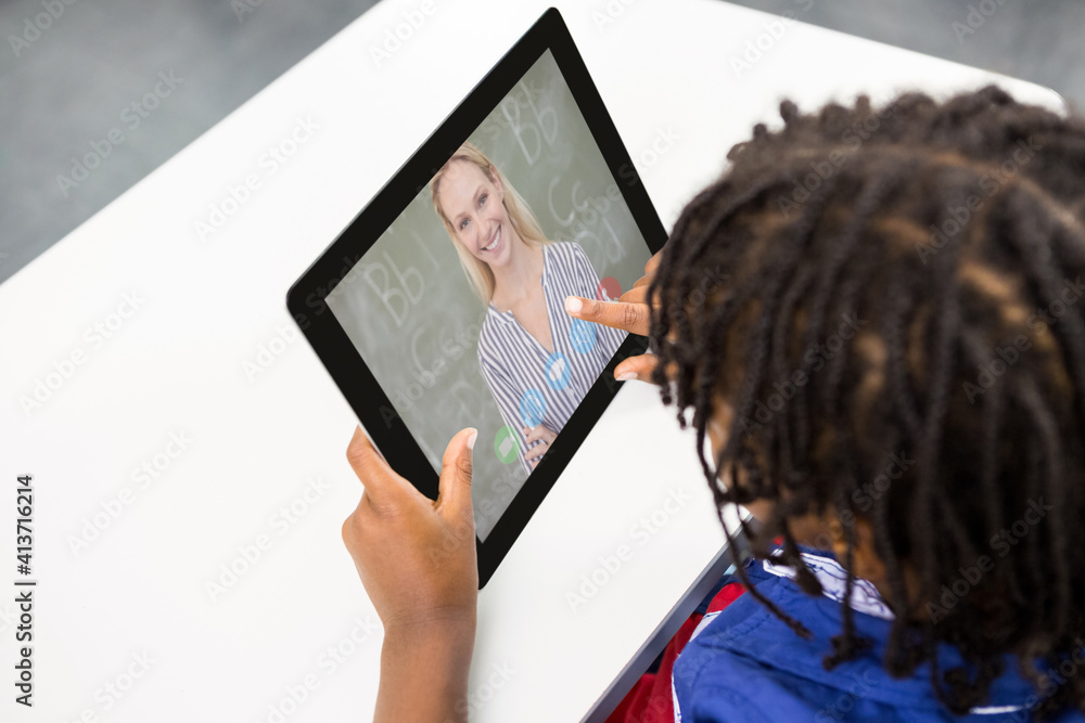 Male student having a video call with female teacher on digital tablet at school