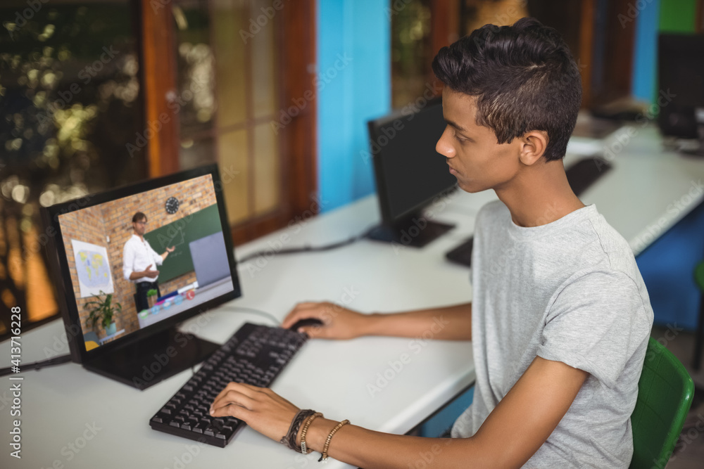 Male indian student having a video call with male teacher on computer at school