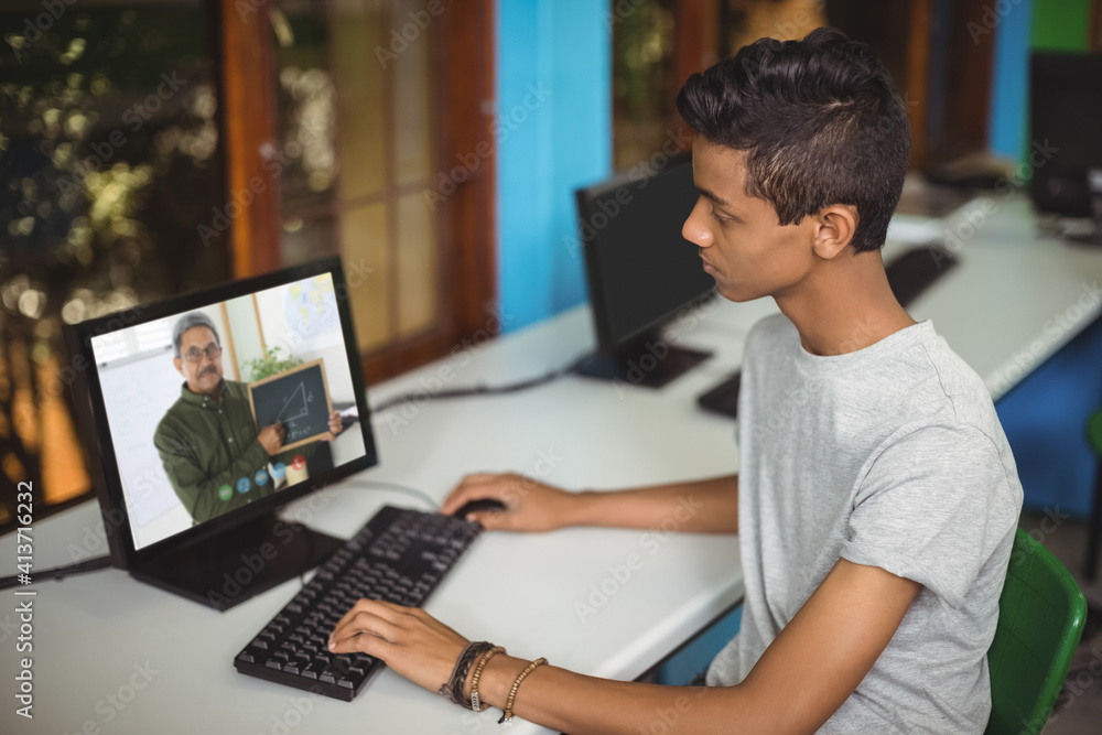 Male indian student having a video call with male teacher on computer at school