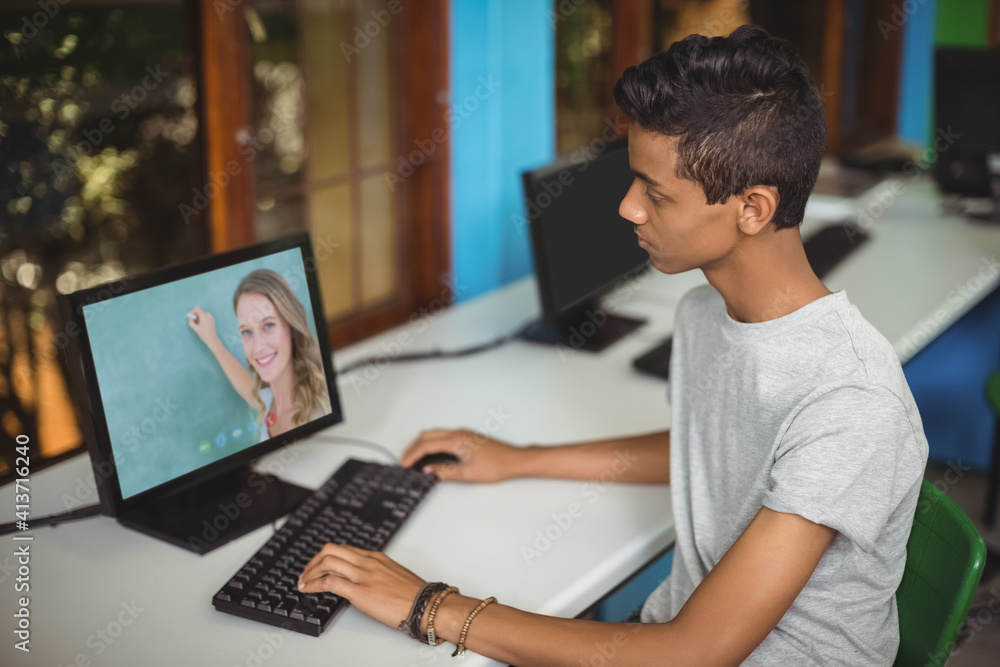 Male indian student having a video call with female teacher on computer at school