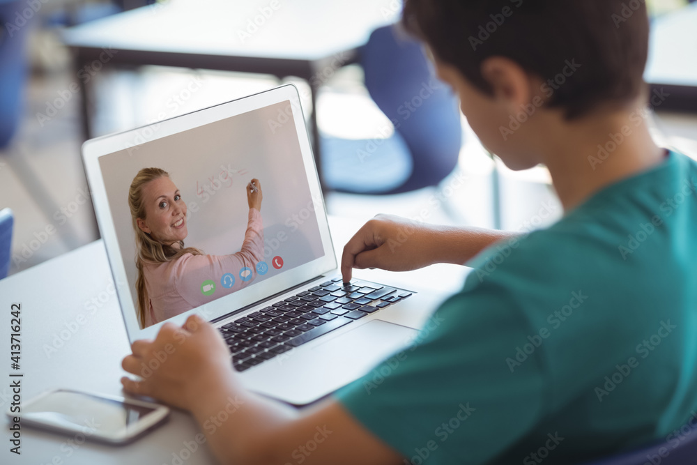 Male caucasian student having a video call with female teacher on laptop at school