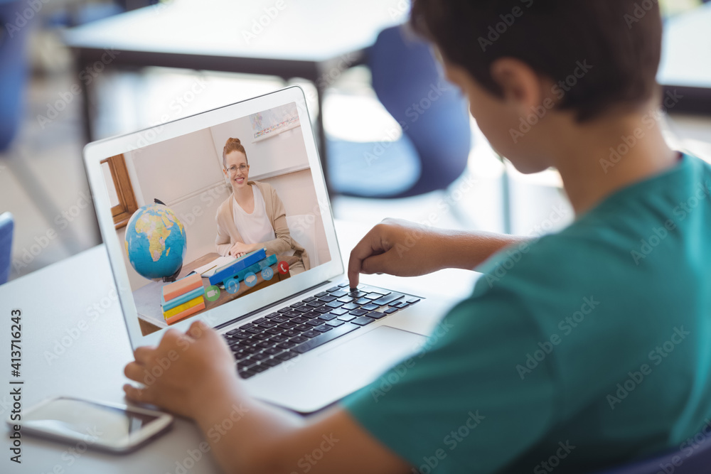 Male caucasian student having a video call with female teacher on laptop at school