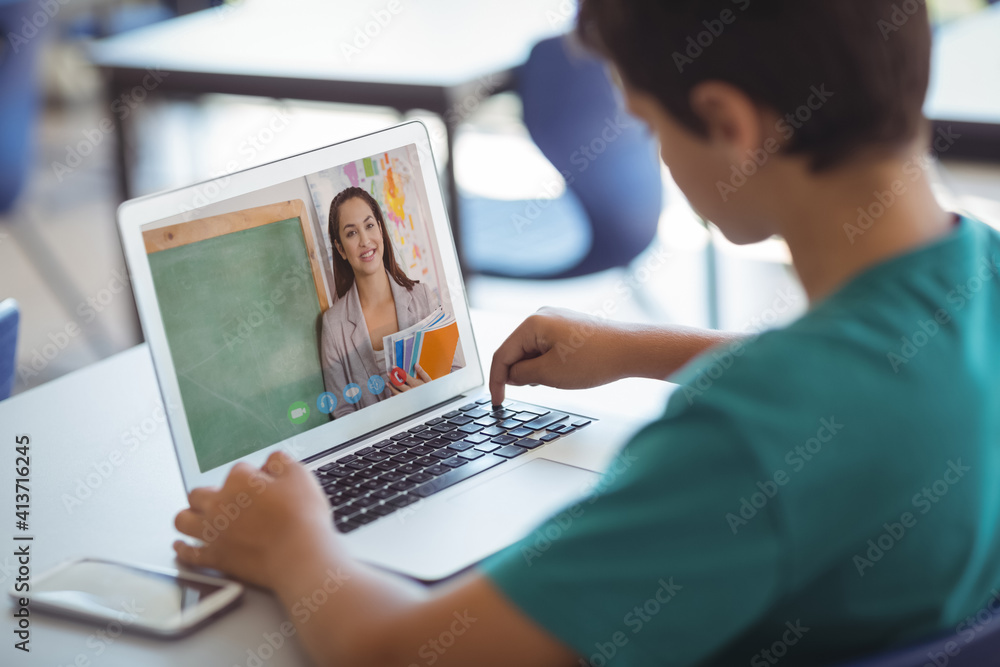 Male caucasian student having a video call with female teacher on laptop at school