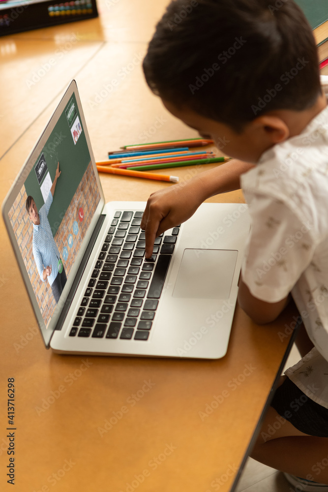 Male student having a video call with male teacher on laptop at school