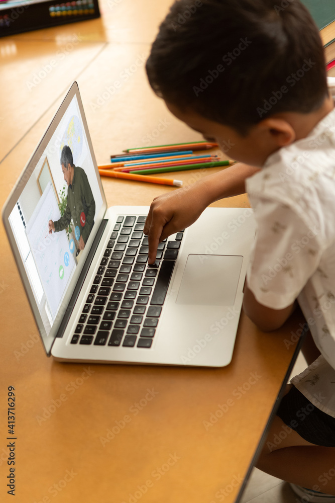 Male student having a video call with male teacher on laptop at school