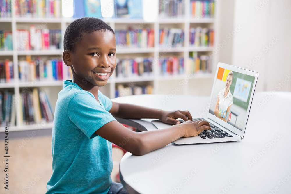 Portrait of male african american student having a video call with female teacher on laptop at libra