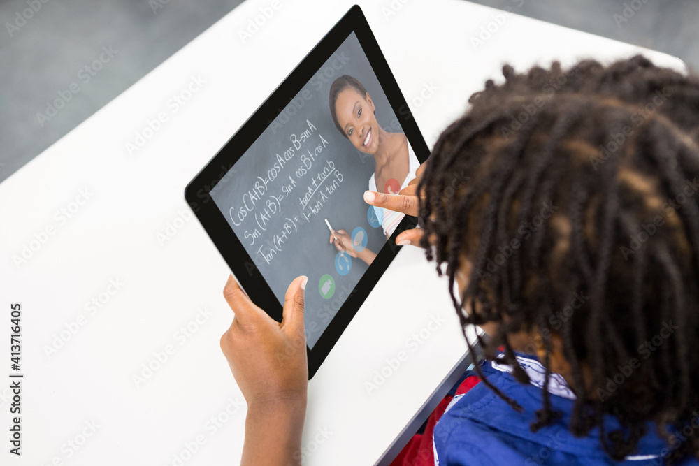 Male student having a video call with female teacher on digital tablet at school