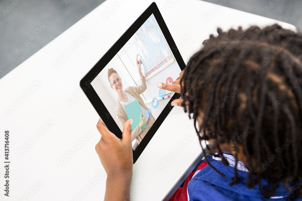 Male student having a video call with female teacher on digital tablet at school