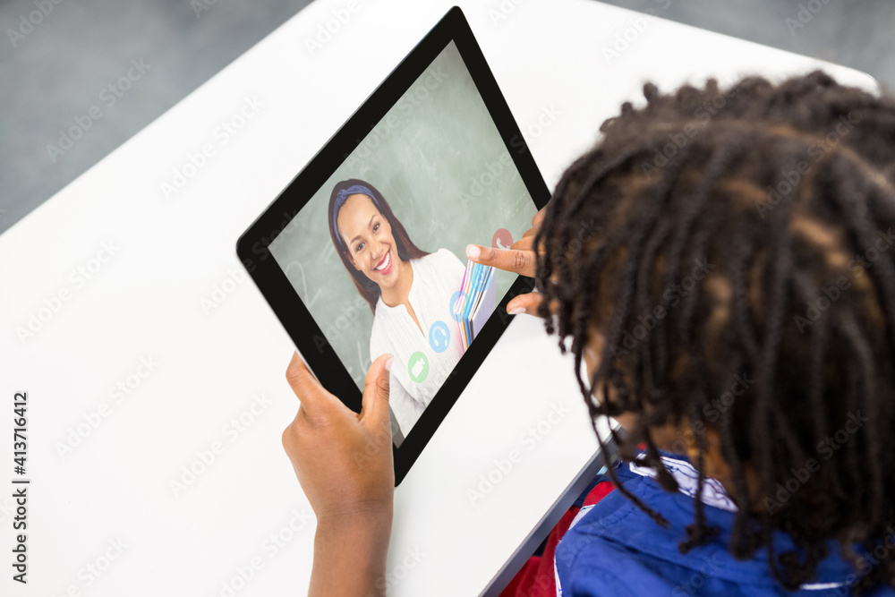 Male student having a video call with female teacher on digital tablet at school