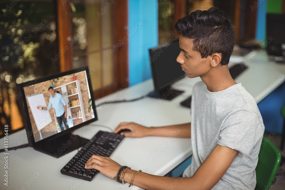 Male indian student having a video call with male teacher on computer at school