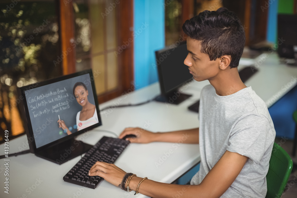 Male indian student having a video call with female teacher on computer at school