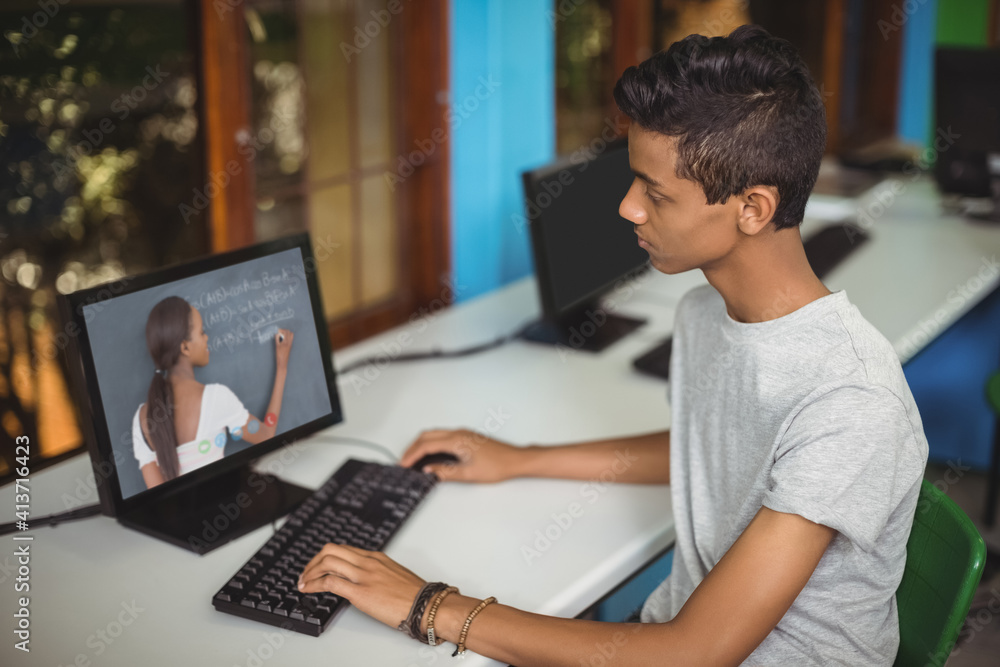 Male indian student having a video call with female teacher on computer at school