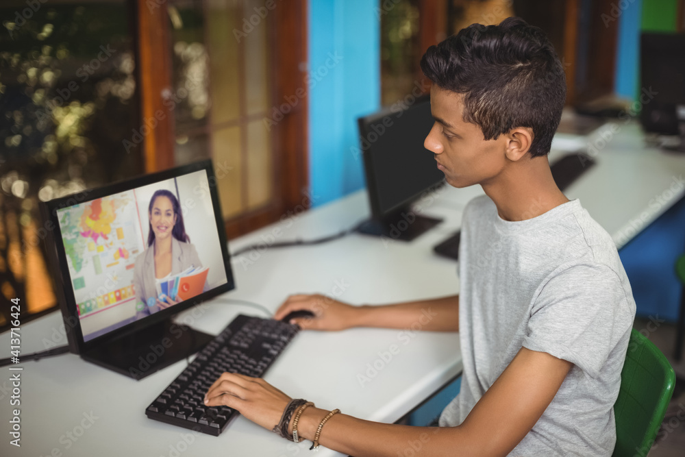 Male indian student having a video call with female teacher on computer at school