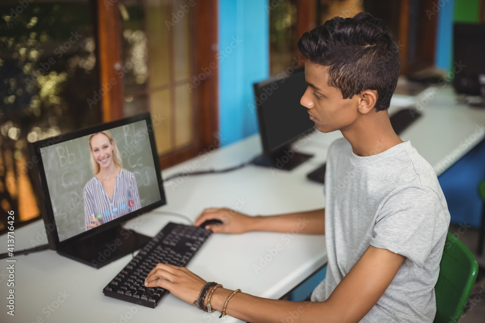 Male indian student having a video call with female teacher on computer at school