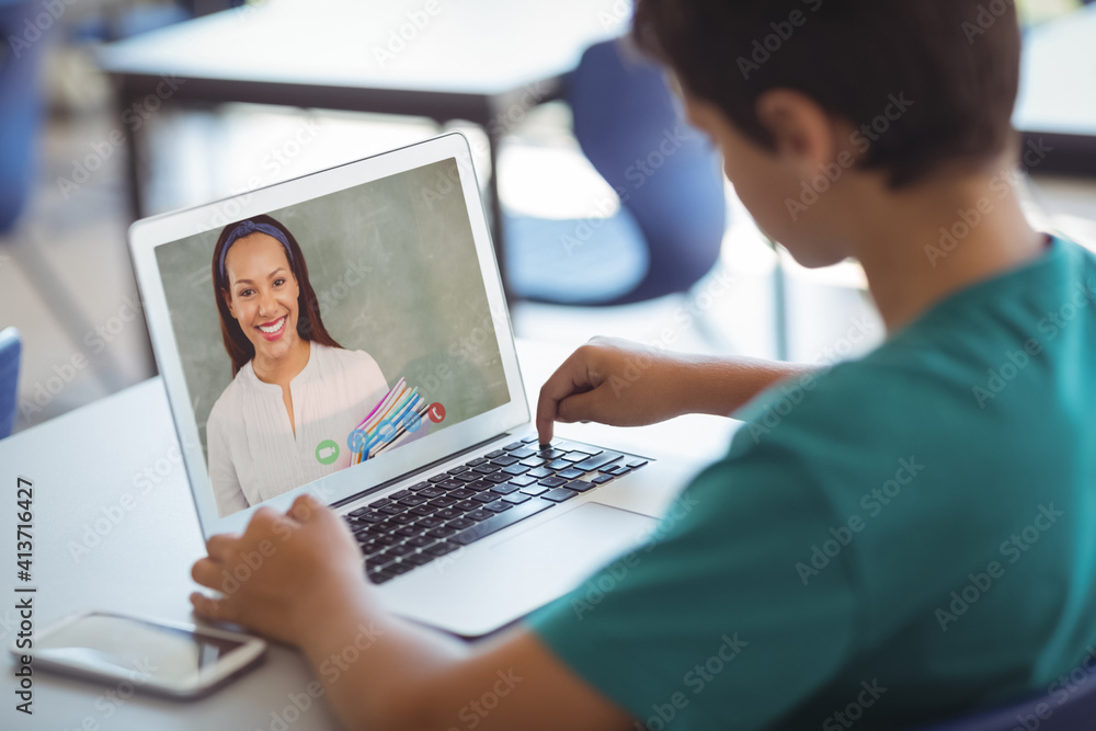 Male caucasian student having a video call with female teacher on laptop at school