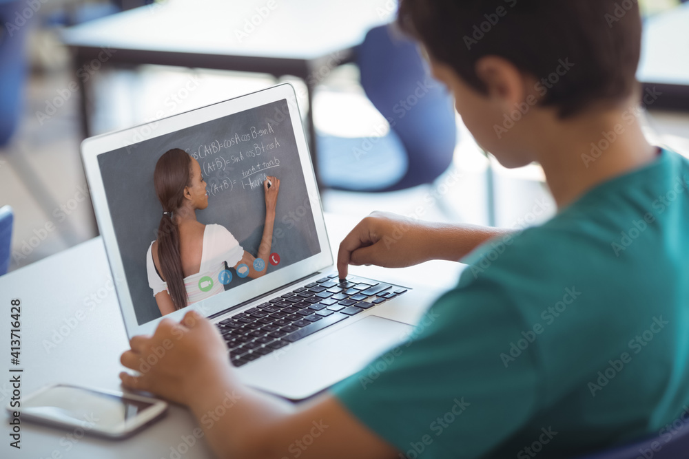 Male caucasian student having a video call with female teacher on laptop at school