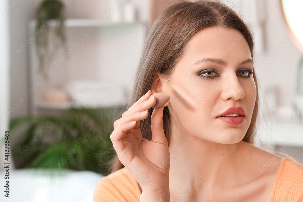 Beautiful young woman applying contouring makeup at home