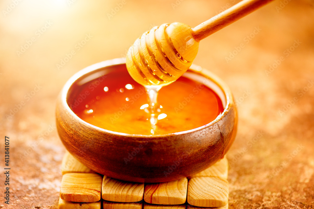 Honey dripping from honey dipper in wooden bowl.  Close-up. Healthy organic Thick honey dipping from