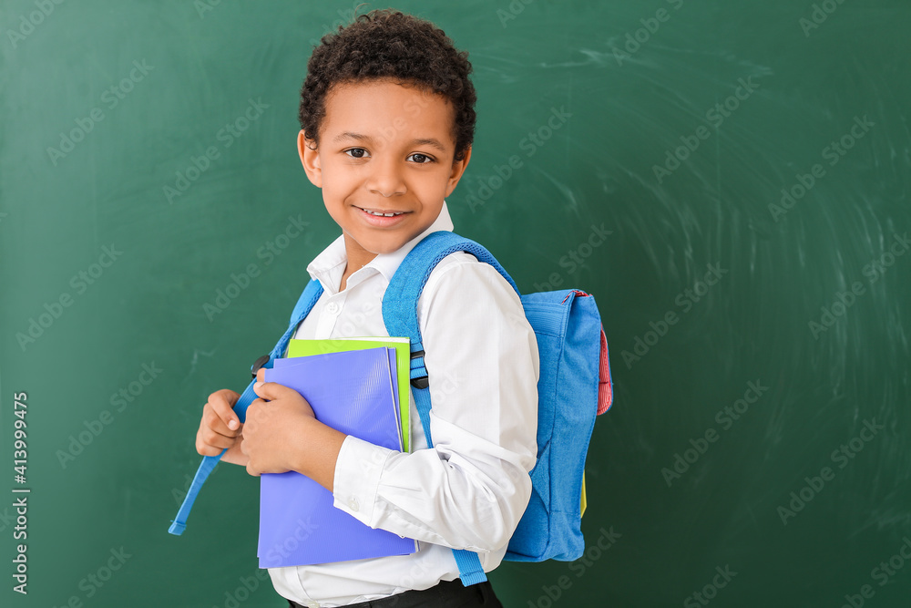 Little African-American schoolboy near chalkboard in classroom