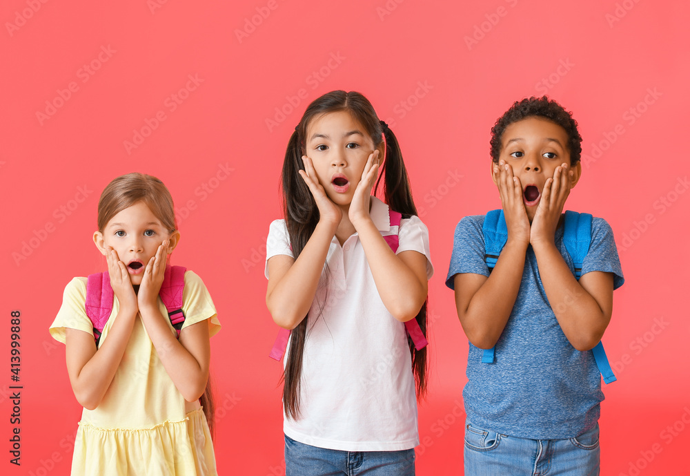 Surprised little schoolchildren on color background