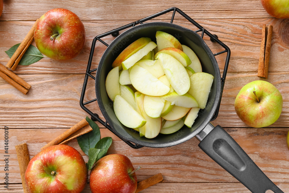 Frying pan with cut apples on wooden background