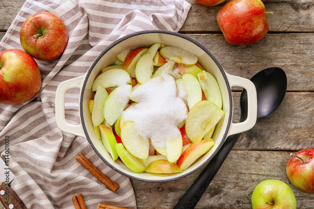 Cooking pot with cut apple and sugar on wooden background