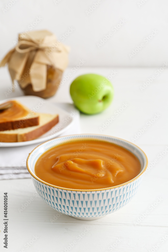 Bowl with sweet apple jam and toasts on light wooden background