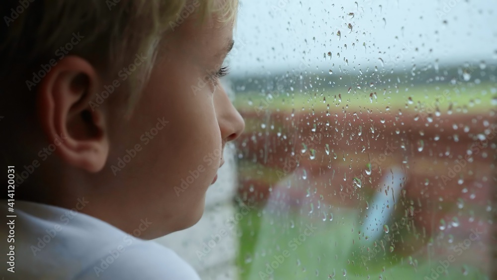 A little boy looks out the window during the rain.