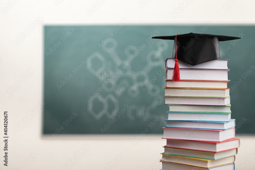 Stack school books with a black graduation hat