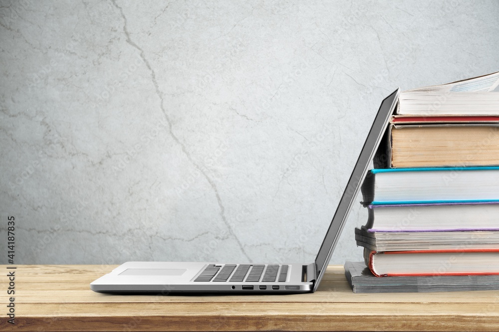 Stack of books with laptop on wooden table