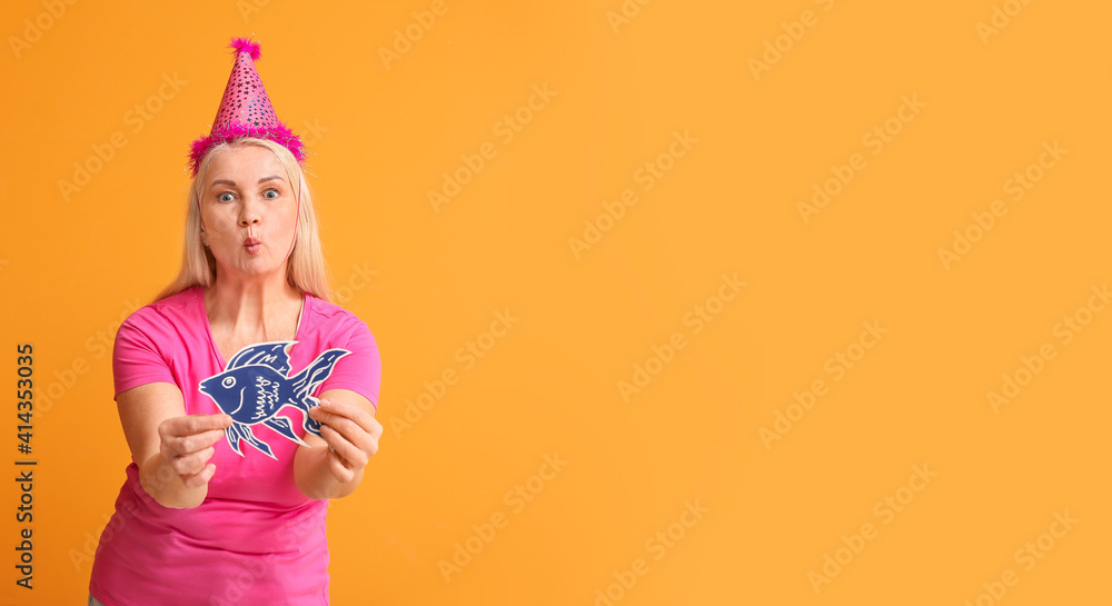 Mature woman with paper fish on color background. April Fools Day celebration